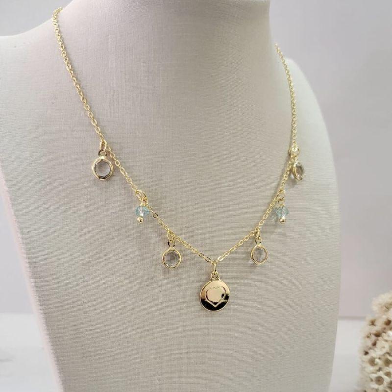 Chocker com uma chapinha redonda com coracao no meio e quatro pedrinhas na cor cristal e duas na cor aqua banhado a ouro 18K TAM35CM